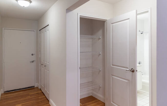 A white pantry with a door open to a bathroom.