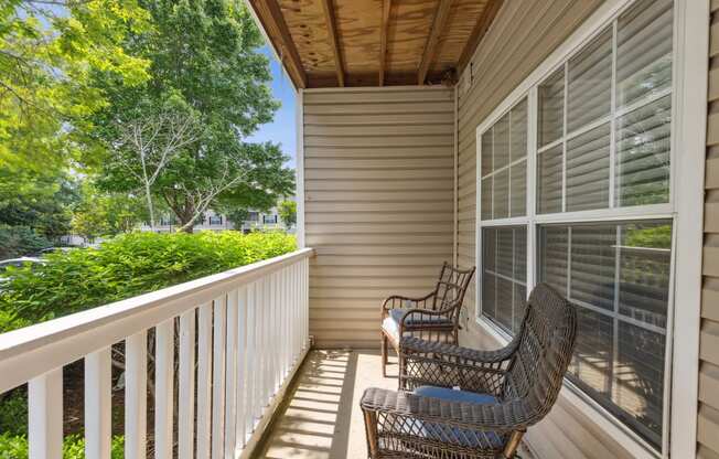 two wicker chairs on a porch with a view of the yard and trees