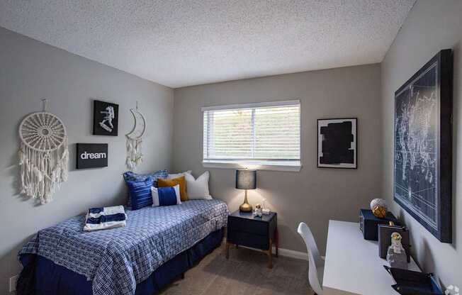 A bedroom with a bed, desk, and a dream catcher hanging on the wall.