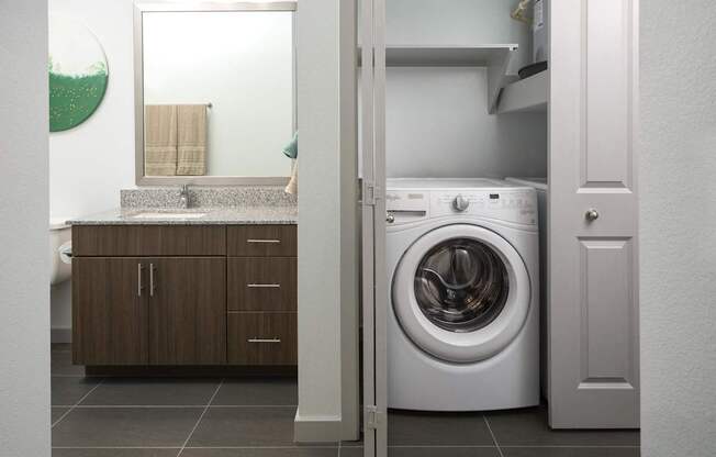 a white washer and dryer in a bathroom with a sink and a mirror