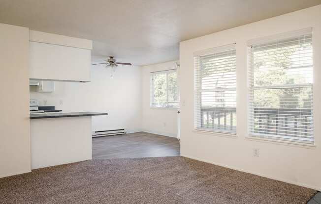 an empty living room with a ceiling fan and large windows