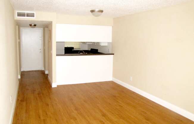 an empty living room with wood floors and a kitchen