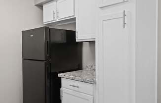 A black refrigerator is in a kitchen with white cabinets.