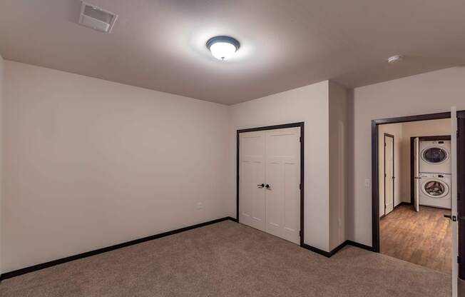 A bright bedroom here at The Park featuring soft carpet, double closet doors, and convenient access to in-unit laundry, creating a comfortable, practical, and inviting private retreat.