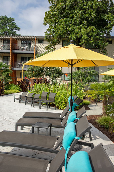 A yellow umbrella is in front of a building and a row of chairs.