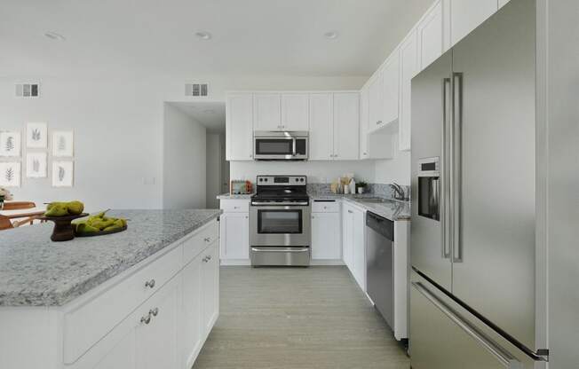 a white kitchen with stainless steel appliances and marble counter tops