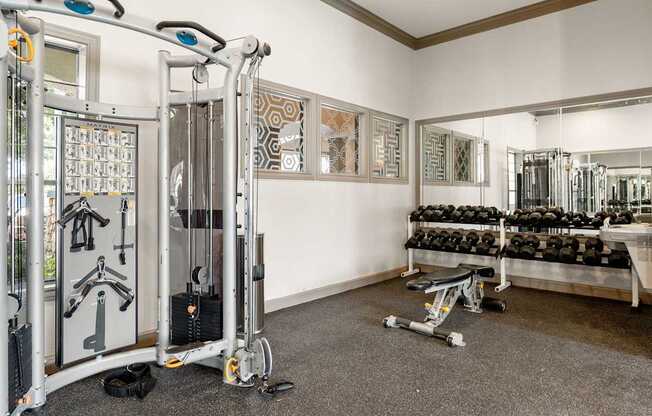 Strength training room with cable machine, dumbbell rack, bench, and full wall mirrors.