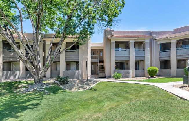 A tree is in front of a building with a lawn in the foreground.