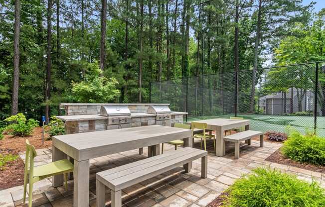 an outdoor patio with a picnic table and grill and a tennis court in the background