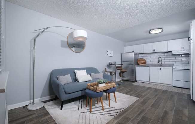 Open concept kitchen and living area in Fusion Fort Worth efficiency apartment with subway tile backsplash and modern lamp over a blue couch.