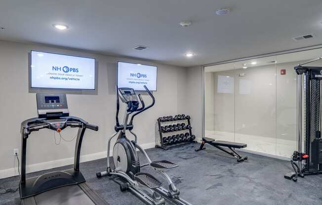 a gym with treadmills and weights and a tv on the wall