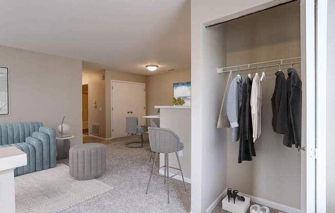 A room with a grey sofa, a white desk, a chair, a clothing rack, and a pair of shoes.