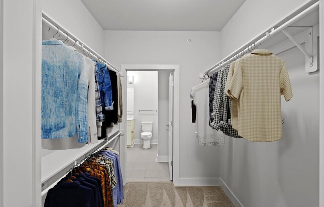 a long white closet with clothes hanging in it and a white bathroom
