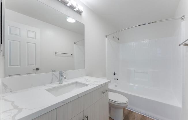 A white bathroom with a sink, toilet, and shower.