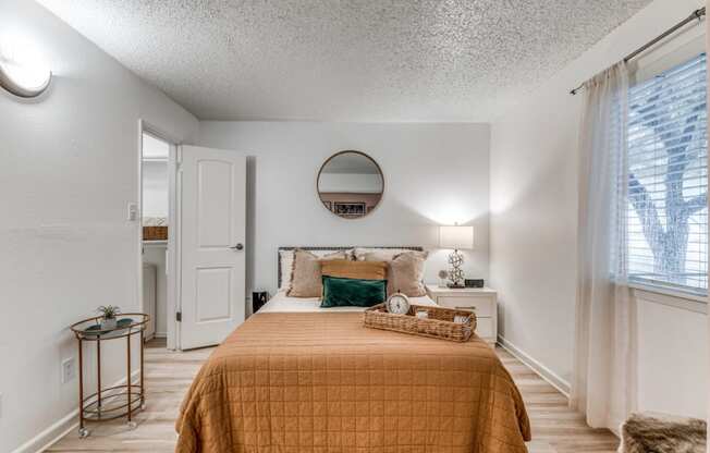 Renovated bedroom in Fusion Fort Worth, previously Desert Sands apartments Large bed with camel duvet and green velvet pillow next to midcentury modern bar cart with succulent.