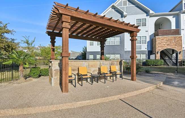 A wooden pergola with yellow chairs is in the foreground of a residential area.