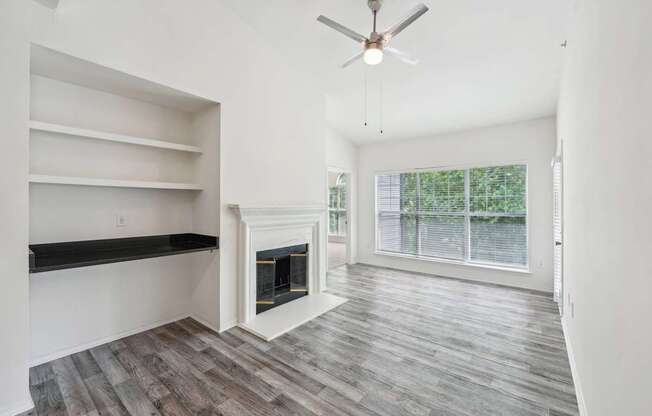A living room with a fireplace, a ceiling fan, and shelving with a desk area.
