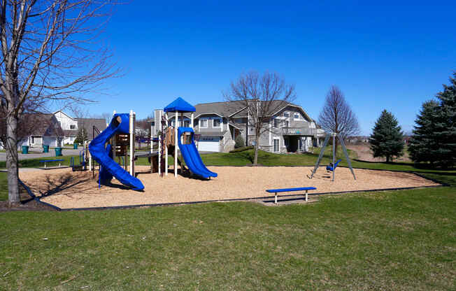 Community playground located on the property for time playing outside. Playground features two slides, a swing set, and multiple options of bench seating along the perimeter.