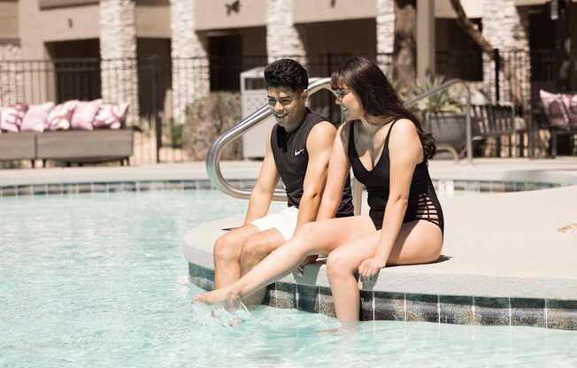 A man and a woman are sitting on the edge of a pool.