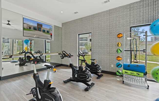 A gym with exercise bikes and a TV screen showing a building.