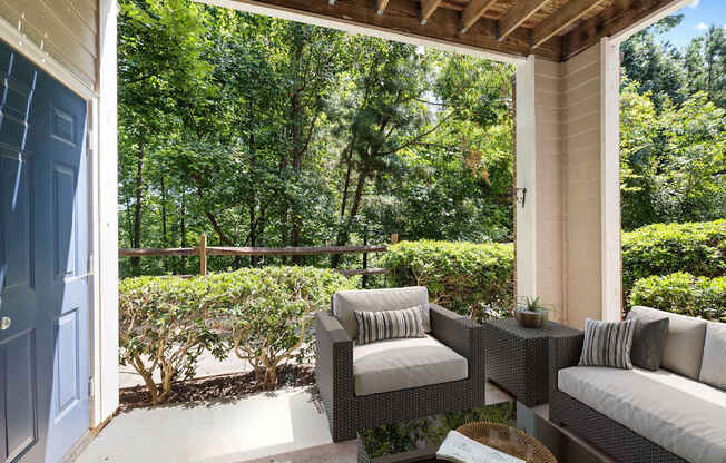 A patio with a couch, chair, and table with a view of a wooded area.