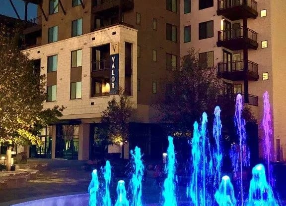 a fountain is lit up at night in front of a building