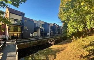 A row of modern buildings line a canal with a wooden walkway alongside.