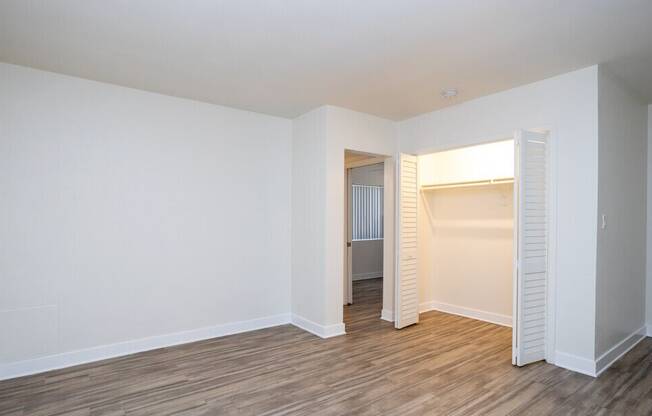 A room with white walls and wooden flooring with a doorway leading to another room.