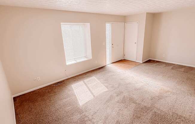 an empty living room with carpet and a door to a bedroom