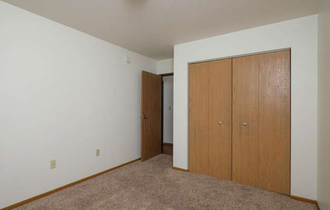 a bedroom with a closet and a door to a hallway. Fargo, ND Park Circle Apartments.