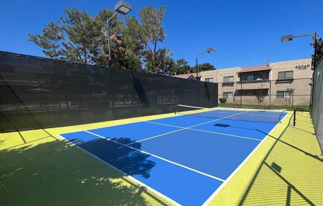 A tennis court with a blue and yellow surface and a black fence surrounding it.