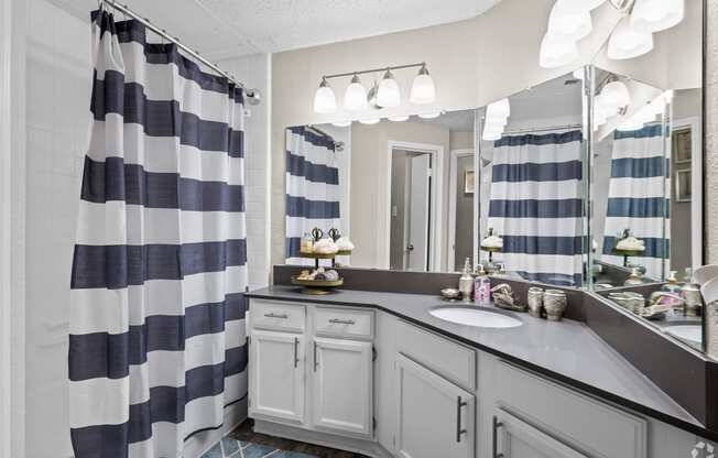 a bathroom with gray cabinets and a blue and white striped shower curtain