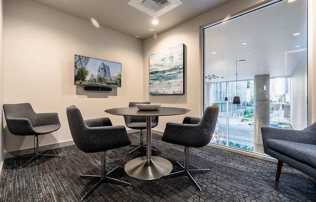 A conference room with a table surrounded by chairs and a television on the wall.