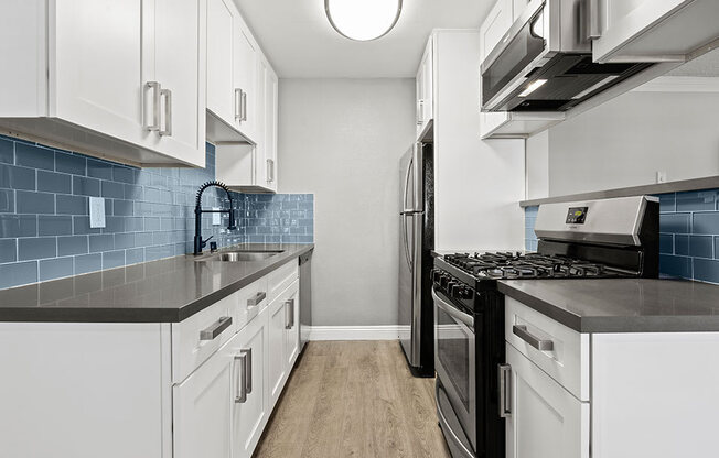 Blue tiled kitchen with stainless steel oven, microwave, and fridge.