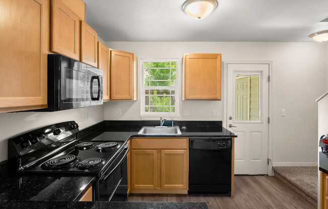 a kitchen with black counter tops and black appliances and wooden cabinets