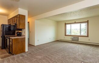 an empty living room with a kitchen and a large window