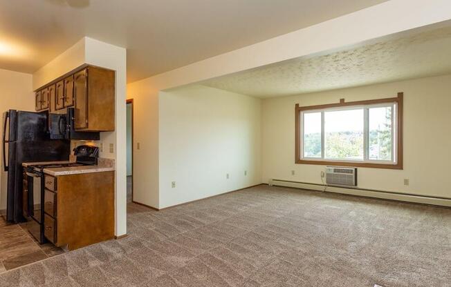 an empty living room with a kitchen and a large window