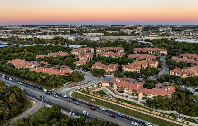A sunset view of a highway with cars driving and apartment buildings on the side. at Bridge at Heritage Woods, Texas, 78753