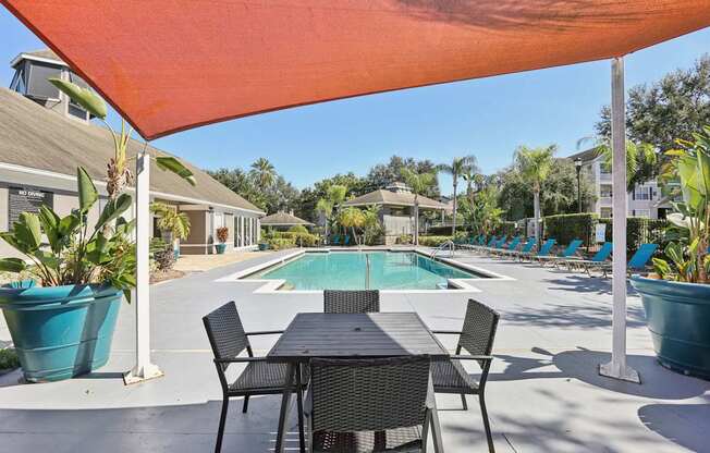 A table and chairs are set up under an orange shade sail.