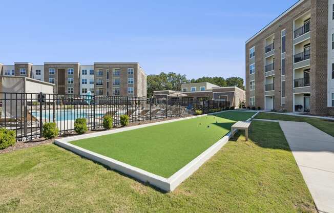 A grassy area in front of apartment buildings with a pool and a small pavilion.