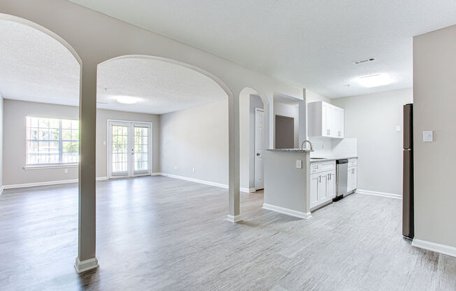 an empty living room with a kitchen in the background