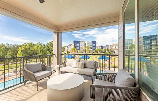 A balcony with a white couch, grey armchair, and a white ottoman.