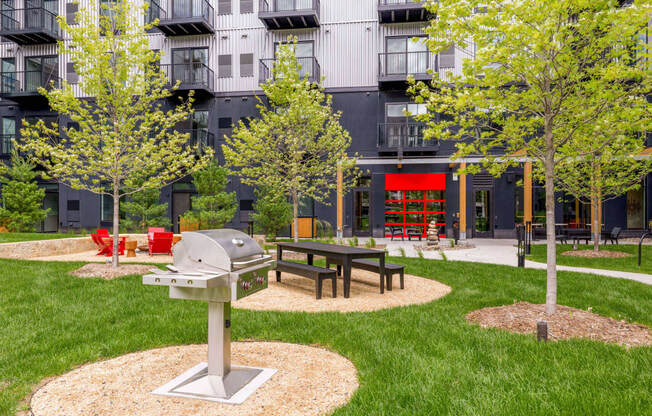 a picnic area with a grill and trees in front of an apartment building