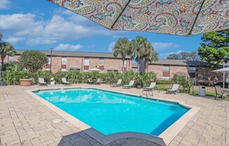 A beautiful sunny day by a pool with a table and chairs under a canopy at Magnolia Apartments in Shreveport, LA