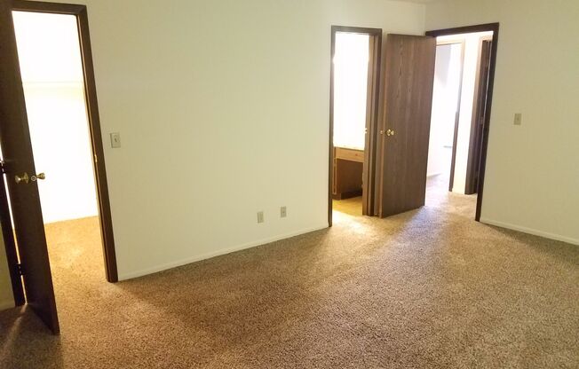 A carpeted room with two doors and a window.