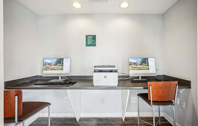 A room with two computer monitors and a printer on a desk.