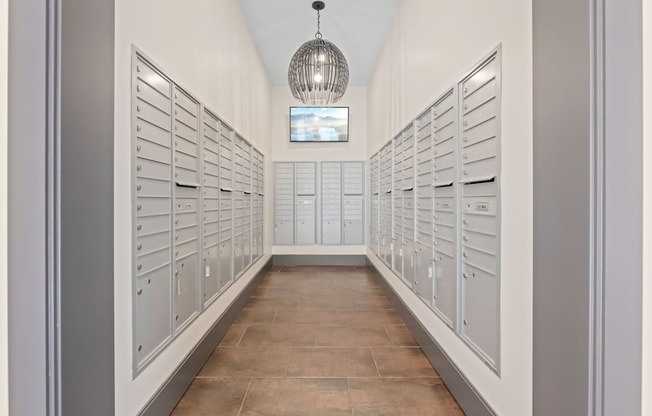 A long hallway with a chandelier and a row of mailboxes on the wall.
