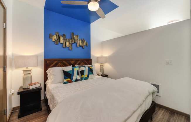 Bedroom with Sliding Door, Hardwood Inspired Floor, White Comforter Bedding, Blue Wall and Ceiling Fan/Light