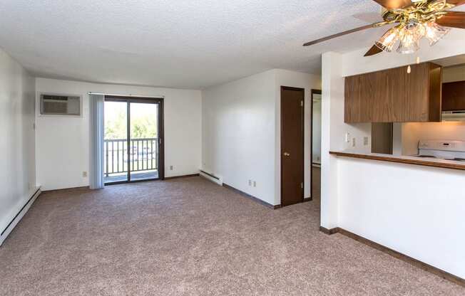 an empty living room with a ceiling fan and a door to a balcony
