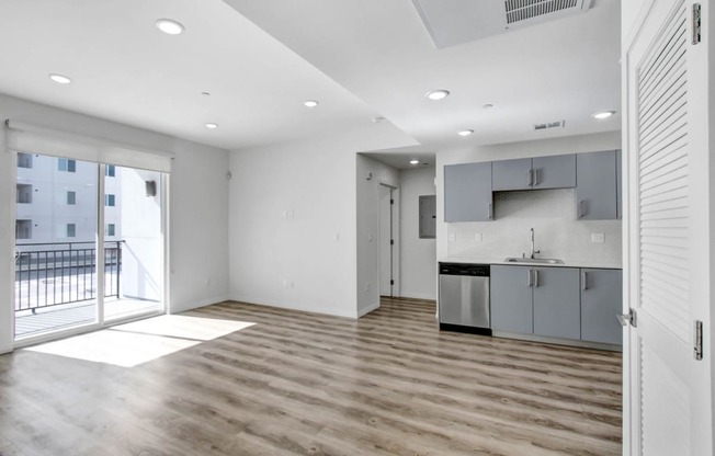 an empty living room with a kitchen and a balcony